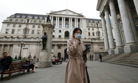 A woman wearing a protective face mask walks in front of the Bank of England.