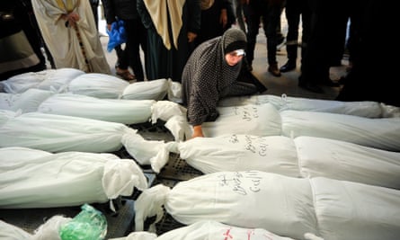 A woman kneels next to a shrouded body