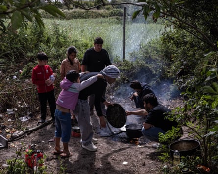 People cooking on a small open fire in a clearing next to a field
