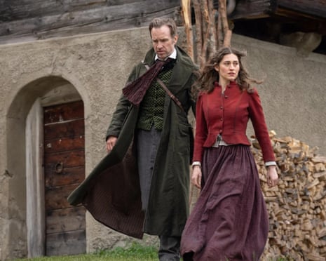 A man and a woman in Victorian dress outside a mountain chalet