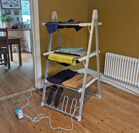 A Dunelm 3-tier A-frame heated airer with clothes draped on it in a ochre room with a wooden floor