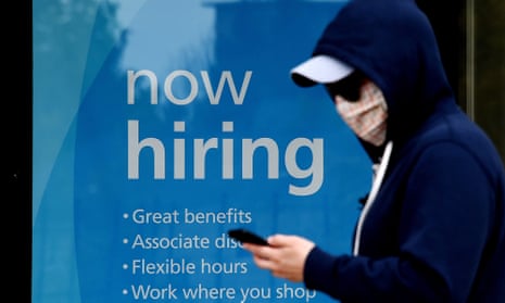 A man wearing a face mask walks past a sign “Now Hiring” in front of a store amid the coronavirus pandemic.