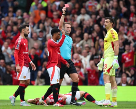 Thomas Bramall shows Emiliano Martínez a red card while Rasmus Højlund lays on the pitch.