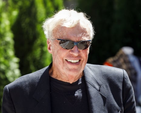 a man in a suit jacket and sunglasses smiles outside