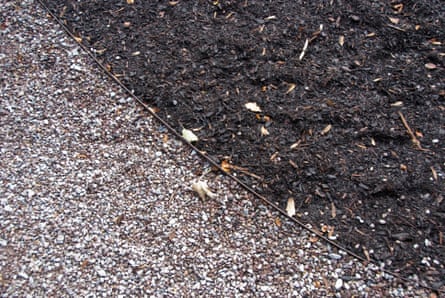 Borders of pebbles and black mulch abut in a garden