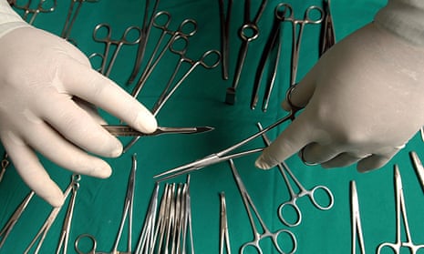 Close-up on the hands of a surgeon holding a scalpel and a pair of forceps over a table laden with various surgical tools.