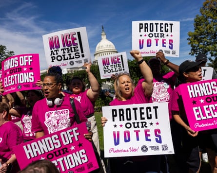 People wearing pink T-shirts hold up signs saying âÂÂProtect Our Votesâ and âÂÂHands Off Our Electionsâ outside at rally
