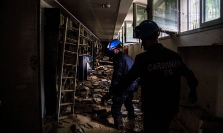 Two carabinieri with safety helmets and head torches in a section of the library filled with water and mud.