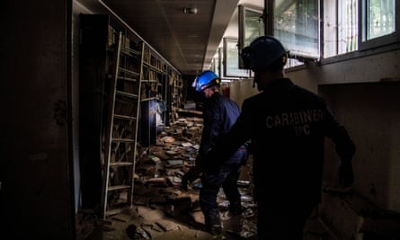 Due carabinieri con caschi di sicurezza e torce frontali in una sezione della biblioteca piena di acqua e fango.