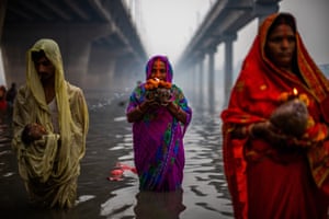 Three women in brightly coloured saris stand in the river