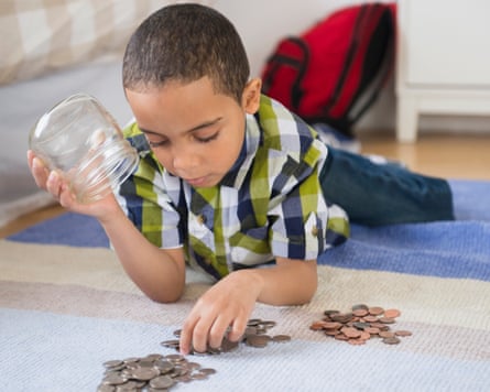 A boy lying on the floor counts coins from a glass jar on a rug