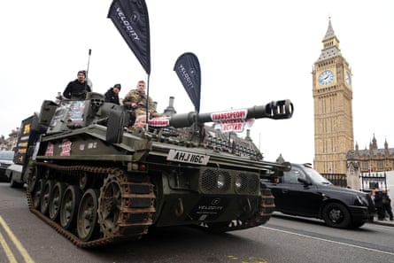 Men drive a tank across Westminster Bridge, with signs saying “tradespeople deserve better”