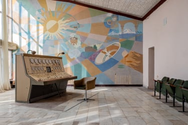 A large console with dials on it in a room with a mural covering the far wall featuring a god-like figure and the sun