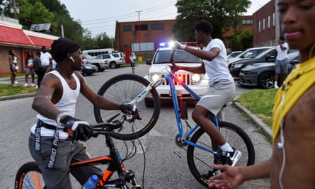 Young people ride their bikes near a police car while they gather in the parking lot of Hip Hop Chicken in Baltimore.