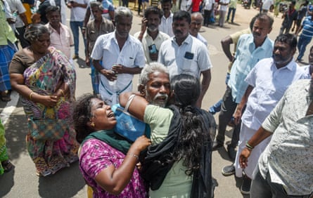 Two women and a man hug each other as others look on