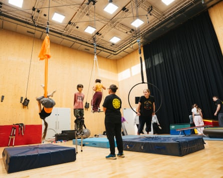 Young people using trapezes over crash mats, as instructors look on