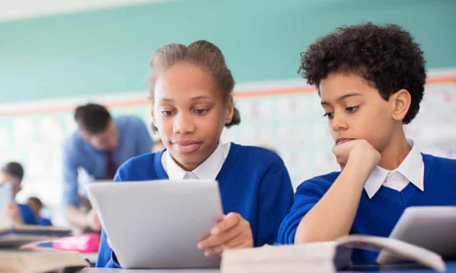 Two black children in school uniforms looking at a tablet screen