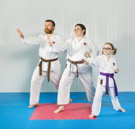 Paul and Katy Greer and their daughter, Lucy, all wearing white karate suits and coloured belts, and standing in line in a karate pose