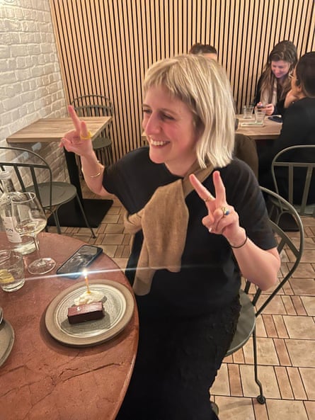 Ellie Violet Bramley makes peace signs with both hands beside a small birthday cake