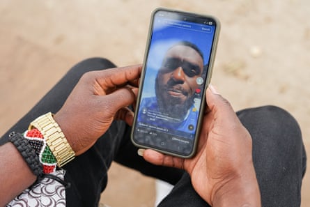 A man’s hands hold a phone. On the screen a man’s face can be seen