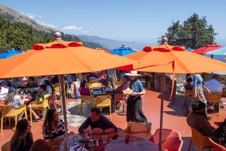 Orange umbrellas over patio tables with the ocean beyond.