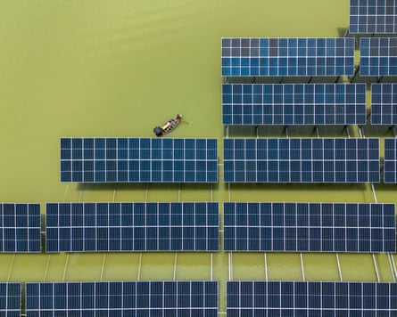 An overhead shot of a wooden fishing boat navigating between solar panels