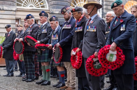 Veteran in uniform stand holding poppy wreaths