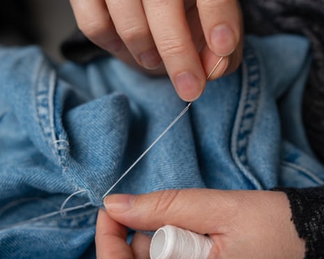 A woman mends jeans by hand with needle and patch on denim fabric