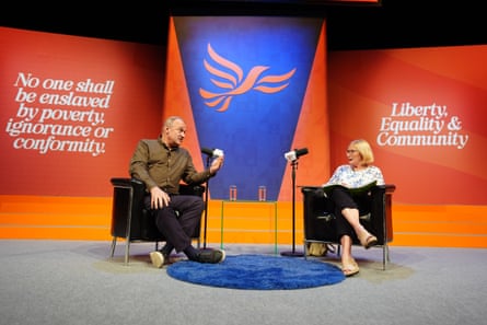 Ed Davey and Carolyn Quinn seated facing on another on a stage with Lib Dems branding