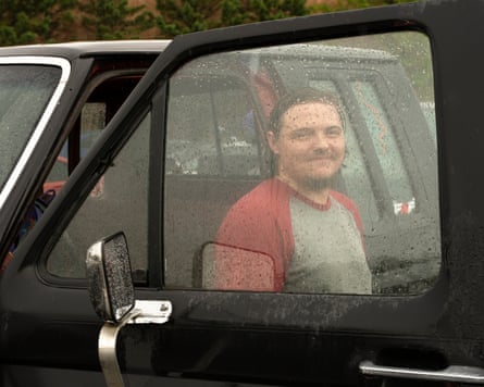 Trey Kemp smiles while sitting inside his truck, viewed through a rain-covered window