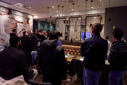 Men standing with their backs to the camera in the venue, watching something