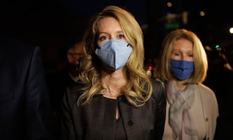 A woman with blonde hair wearing a blue mask looking into the camera.