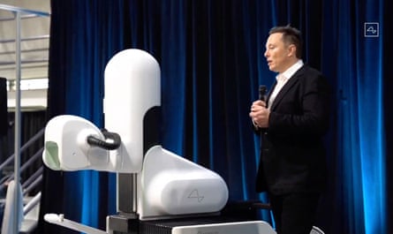 Elon Musk next to a surgical robot during a 2020 presentation. Robot consists of white domed and curved shapes