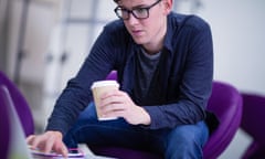 Student holding coffee cup and using computer.