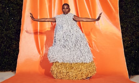 Issa Rae in a wide feathered dress, her arms reaching out to the sides