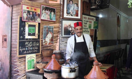 Cook, wearing a red fez hat, tends tagines at the street-food stall Terrasse Bakchich in Marrakech, Morocco.