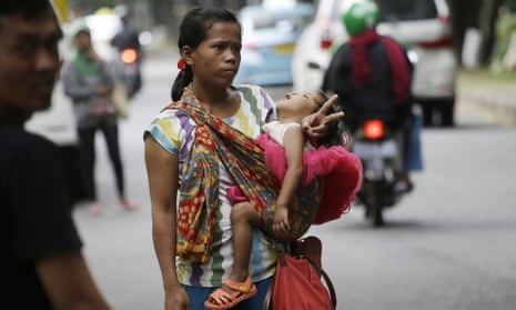 A woman carries her baby as she signals to show that she’s for hire as a ‘jockey’ to help drivers cheat a peak time traffic rule of three people to one car during rush hour in Jakarta, Indonesia.