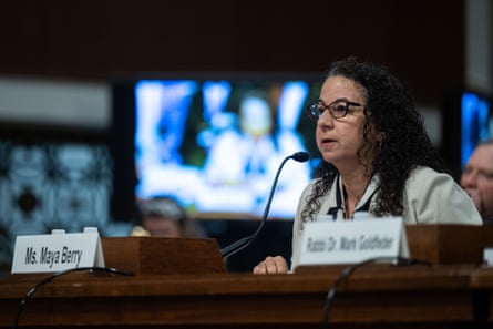 a woman speaks into a microphone while seated at a table