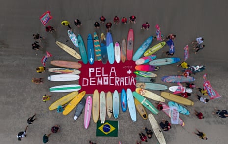 Aerial view of surfers and their colourful surfboards circling a banner reading ‘For Democracy’ at a Brazil rally