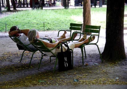 A couple sit reclined in the shade in a park with their feet on chairs