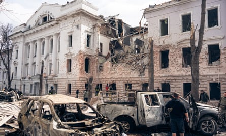 Burnt out cars in the foreground with a destroyed building in the background