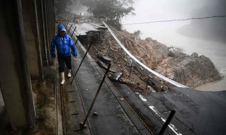 A man walks by a collapsed road caused by heavy rain in Kuma, Kumamoto prefecture. Flooding and heavy rains have killed 58 people.