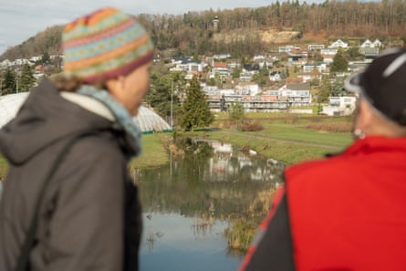 A view of a body of water surrounded by grass and houses taken over the shoulders of two people.