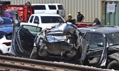 A vehicle is seen off to the side of a set of train tracks, its back end destroyed and all four doors open.