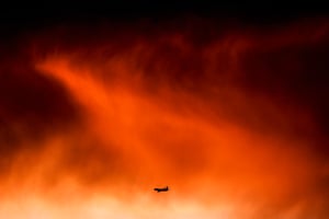 A passenger plane is dwarfed by a big red storm cloud at sunset
