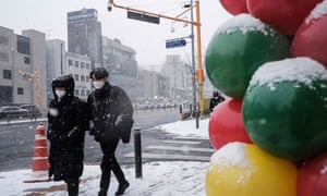 Pedestrians walk on a pavement as it snows in Seoul on 18 December as South Korea reports a record number of people admitted to hospital with serious Covid-19 symptoms and in critical condition.