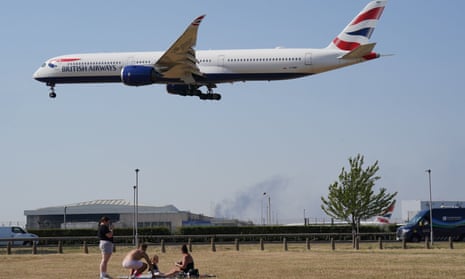 People enjoy the hot weather in a field beneath a British Airways flight coming into land at Heathrow airport, London on 19 July 2022