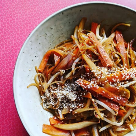 A close-up of a bowl of stir-fried noodles with carrots, bean spouts and a sprinkling of sesame seeds.