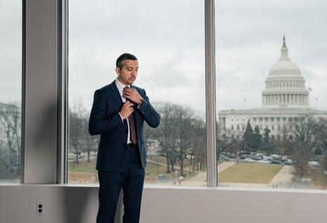hasan straightens tie at window with view of capital