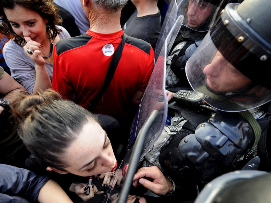 Jasmina Golubovska does her lipstick in the shield of a policeman in front of a government building in Skopje, Macedonia, on  5 May, 2015